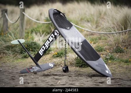 Une planche de surf hydrofoil en fibre de carbone avec hydrofoil en fibre de carbone et laisse se trouve sur le sable à Piha Beach, Auckland, Nouvelle-Zélande. Banque D'Images
