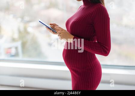Femme enceinte utilisant un smartphone pendant la grossesse pour acheter des vêtements de maternité, en utilisant l'application grossesse, faire un bilan de santé rendez-vous des médecins Banque D'Images