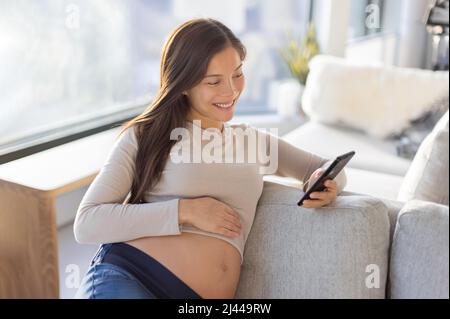 Femme asiatique enceinte heureuse d'utiliser l'application de téléphone mobile pour faire du shopping ou de la télémédecine. Grossesse style de vie à la maison Banque D'Images