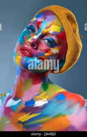 La vie consiste à utiliser toute la boîte de crayons. Photo studio d'une jeune femme posant avec de la peinture multicolore sur son visage et un chapeau français sur sa tête. Banque D'Images