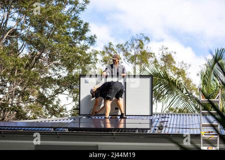 Installation de panneaux photovoltaïques solaires sur une maison de Sydney en tant que deux installateurs mâles s'adaptent aux panneaux REC noirs d'une maison australienne, Sydney, Nouvelle-Galles du Sud Banque D'Images