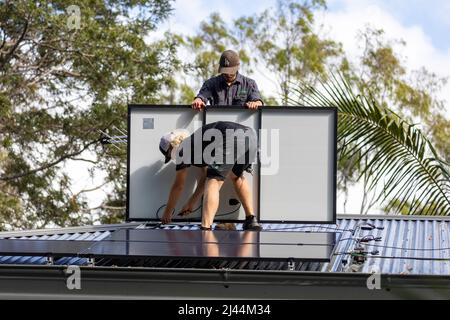 Installation de panneaux photovoltaïques solaires sur une maison de Sydney en tant que deux installateurs mâles s'adaptent aux panneaux REC noirs d'une maison australienne, Sydney, Nouvelle-Galles du Sud Banque D'Images