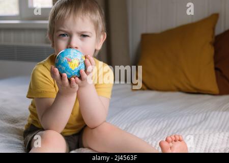 Enfant garçon aux cheveux blonds embrassant le globe terrestre, Save Earth concept. modèle de globe pour enfant de 3 ans. Bébé tout-petit. Développement de l'éducation des enfants Banque D'Images