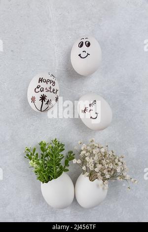 Composition de Pâques. Œufs blancs aux visages amusants peints sur la table. Un petit bouquet dans un œuf. Le concept minimal de Pâques. Une carte de Pâques avec un Banque D'Images