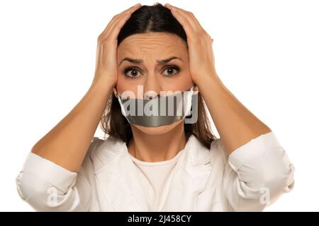 Jeune femme malheureuse avec du ruban adhésif sur sa bouche sur un fond blanc Banque D'Images