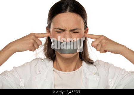 bouleverser la jeune femme avec du ruban adhésif au-dessus de sa bouche bloquant ses oreilles feth les doigts sur fond blanc Banque D'Images