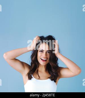 Oubliez la bonne journée de cheveux, je vous présente une journée de cheveux impressionnante. Photo en studio d'une jeune femme attrayante se sentant joyeuse sur fond bleu. Banque D'Images