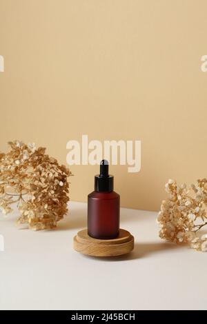 Flacon compte-gouttes en verre ambré sur podium en bois avec fleurs sèches sur fond beige. Design d'emballage de produits de beauté naturels, marquage. Banque D'Images