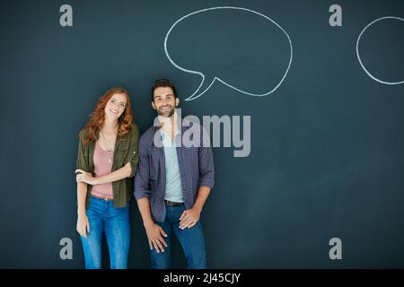 Elle aime un homme qui parle son esprit. Portrait d'un jeune couple debout devant un tableau noir avec des bulles de parole dessinées dessus. Banque D'Images