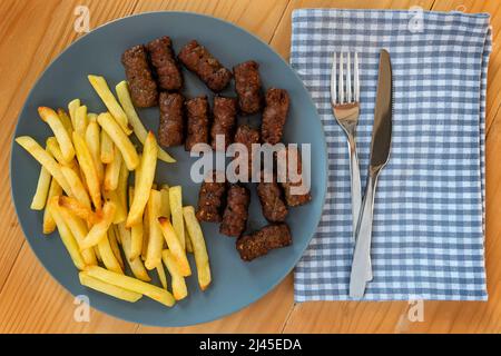 CEVAPi, plat traditionnel de viande hachée des balkans, servi avec des frites dans une assiette bleu marine sur une table en bois Banque D'Images