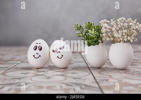 Composition de Pâques. Œufs blancs aux visages amusants peints sur la table. Un petit bouquet dans un œuf. Le concept minimal de Pâques. Une carte de Pâques avec un Banque D'Images