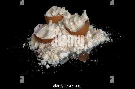 Tas de poudre de protéine d'œuf et coquilles d'œuf isolées sur fond noir avec réflexion miroir sur la table. Nutrition sportive. Banque D'Images