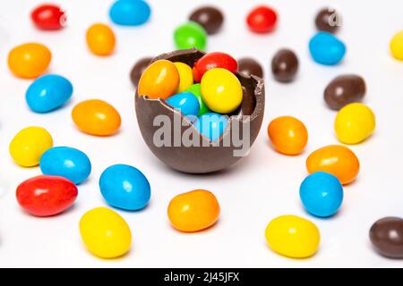 La moitié d'un œuf de chocolat craqué rempli de bonbons multicolores sur un fond blanc avec des bonbons multicolores, vue du dessus. Gâteries pour enfants. SWE Banque D'Images