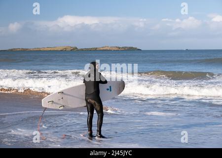 Surfeur tenant une planche de surf portant une combinaison de plongée se préparer à affronter les vagues des White Rocks près de Portrush dans Co. Antrim, Irlande du Nord. Banque D'Images