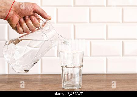 La main d'un homme verse de l'eau pure fraîche de la bouteille dans un verre sur la table, concept de santé et de régime Banque D'Images