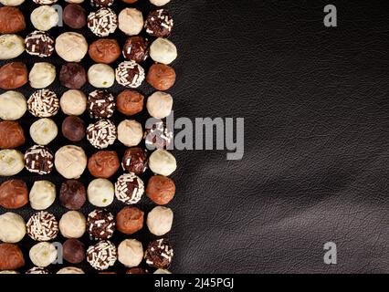 Pralines au chocolat, vue de dessus de diverses pralines au chocolat isolées sur fond de cuir noir à moitié. Banque D'Images