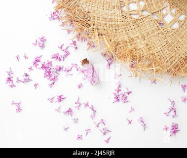 Bouteille transparente avec fleurs lilas debout près d'un chapeau de paille sur fond blanc Banque D'Images