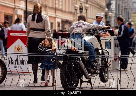 Un jeune garçon joue sur une moto garée dans la rue, Moscou, Russie, mai 1990. Banque D'Images