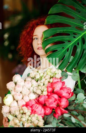 Portrait d'une belle fille au poil rouge avec un bouquet de fleurs printanières dans ses mains, cachant une partie de son visage derrière une feuille verte avec une fleur Banque D'Images