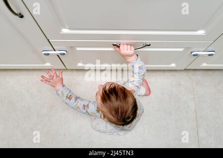 Bébé garçon se déporte d'un tiroir de cabinet avec sa main. L'enfant tient la poignée de la porte de l'armoire, petit enfant Banque D'Images