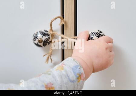 Bébé garçon se déporte d'un tiroir de cabinet avec sa main. L'enfant tient la poignée de la porte de l'armoire, petit enfant Banque D'Images