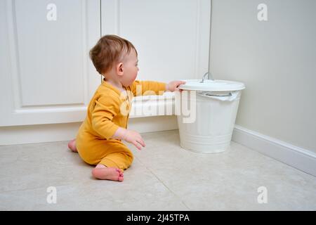 Bébé garçon ouvre une poubelle avec les déchets ménagers. Problèmes de sécurité des enfants dans la chambre d'accueil, petit enfant Banque D'Images