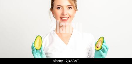 Portrait de jeune femme souriante médecin nutritionniste avec fruits bio avocat posant à l'appareil photo sur fond blanc, espace copie. Les avantages d'une nutrition appropriée Banque D'Images