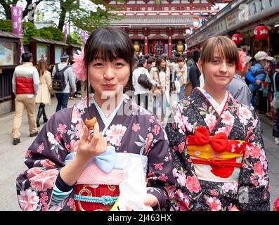 Japon. Tokyo. Une fille japonaise goûtant des bonbons dans les rues d'Asakusa avec son ami occidental Banque D'Images