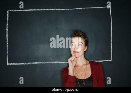 Les pensées peuvent encadrer qui vous êtes. Photo studio d'une jeune femme réfléchie posant avec une illustration craie d'une boîte sur un fond sombre. Banque D'Images