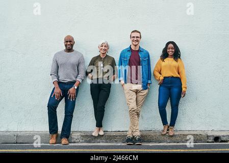 Rien ne peut nous y opposer. Photo en longueur d'un groupe d'hommes d'affaires debout en ligne contre un mur à l'extérieur. Banque D'Images