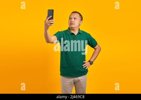 Portrait d'un jeune homme asiatique confus utilisant un téléphone portable lorsqu'il n'est pas connecté à un réseau Internet sur fond jaune Banque D'Images
