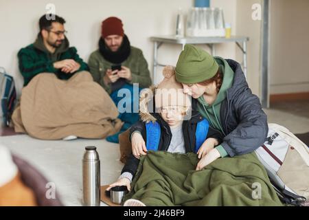 Portrait d'une jeune femme caucasienne embrassant son fils en se cachant dans un refuge pour réfugiés et assise sur un sol recouvert de couvertures, espace pour les copies Banque D'Images