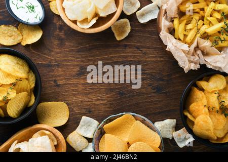 Aliments ou collations malsains. Tous les en-cas classiques de pommes de terre avec des arachides, du pop-corn et des rondelles d'oignon et des bretzels salés dans des assiettes à bol sur fond de bois ancien. Banque D'Images