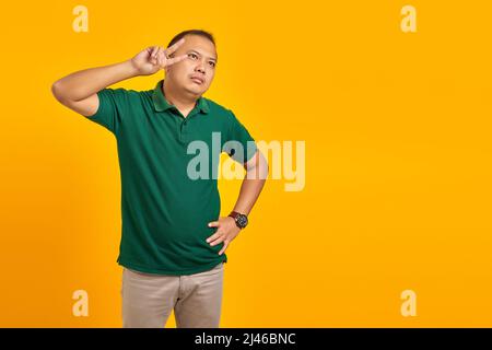 Portrait du triste jeune asiatique faisant signe de paix avec les doigts sur fond jaune Banque D'Images
