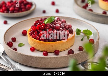 Tartes aux baies fraîches avec baie de cowberry, sucre en poudre et menthe dans une assiette sur table blanche. Dessert savoureux. Gros plan Banque D'Images