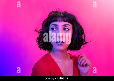 Jeune femme avec chemise rouge regarde le côté surpris. Portrait d'une femme moderne souriante avec un look tendance et des couleurs vives. Banque D'Images