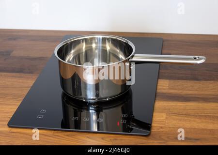 Louche de casserole sur une plaque à induction intégrée dans un plan de travail de cuisine en bois Banque D'Images