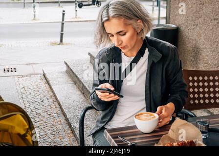 Mère est assise à une table dans un café de rue près d'une poussette Banque D'Images