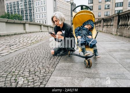 Une femme écrit un message assis près d'une poussette avec son fils endormi Banque D'Images