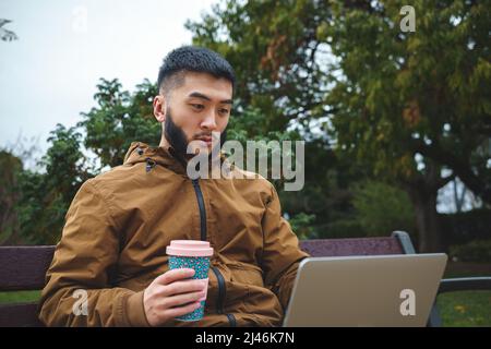 Travailleur indépendant ethnique sérieux travaillant sur ordinateur portable et buvant du café Banque D'Images