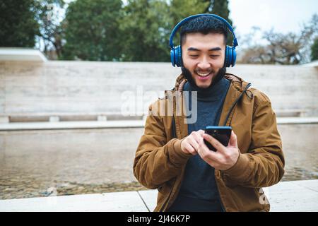 Homme ethnique souriant utilisant un smartphone tout en écoutant de la musique Banque D'Images