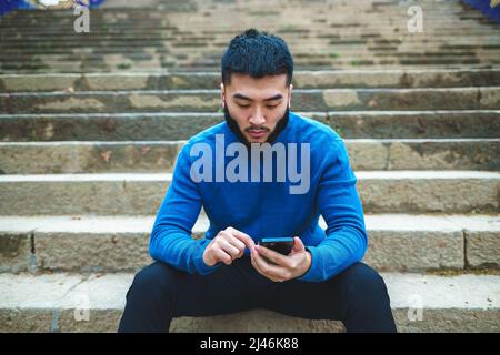 Homme ethnique sérieux utilisant un smartphone sur des escaliers en pierre Banque D'Images