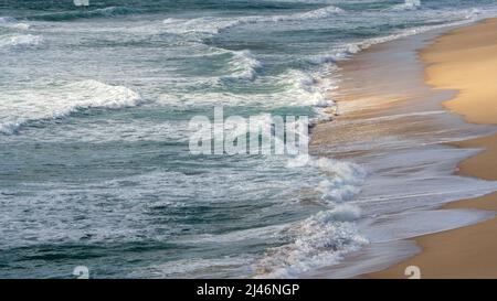 Les vagues de l'océan se jettent sur une plage de sable, créant des motifs de mousse doux le long du rivage. La lumière naturelle et le mouvement doux donnent à la scène côtière un calme, rel Banque D'Images