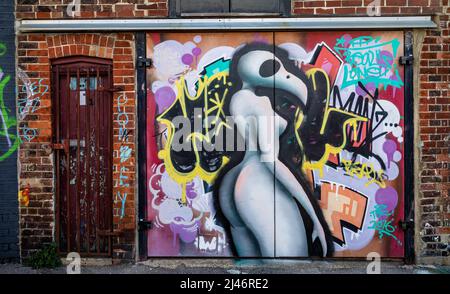 Des graffitis d'art de rue colorés sur les portes de garge à côté d'une porte fermée à clé et rouillée derrière le parc Fratton, le stade appartenant à Portsmouth FC Banque D'Images