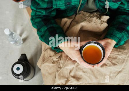 Vue de dessus vue rapprochée du réfugié tenant une tasse de thé chaud tout en se cachant dans un abri pendant la guerre ou la crise, salle de copie Banque D'Images