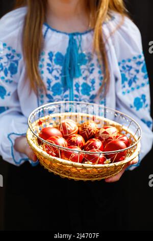 Défocus ukrainian girl dans vyshyvanka tenant panier d'oeufs rouges colorés sur fond noir. Pâques, Ukraine. Œufs artisanaux. Collection de pysanka ou kra Banque D'Images