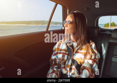 Jeune femme élégante assise sur le siège arrière dans la voiture de taxi et regardant par la fenêtre Banque D'Images