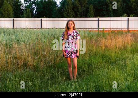 Recentrer la belle adolescente souriante en robe debout sur fond vert d'été. Fille élevée de 12 ou 13 ans sur la pelouse d'été. Hors foyer. Banque D'Images