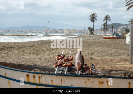 Cuisine typique de la côte andalouse: Sardines, pieuvre et poisson rôtis par un feu de charbon dans un bateau Banque D'Images