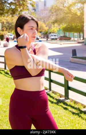 Une jeune athlète de race blanche effectuant des exercices d'étirement dans la rue. L'arrière-plan n'est pas mis au point et le cadrage est vertical. Banque D'Images